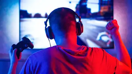 Un joueur avec casque tient une manette devant un écran de jeu éclairé en bleu et rouge.