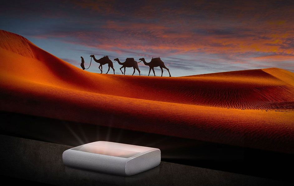 Un projecteur blanc illumine une image de désert avec des dunes orange et une caravane de chameaux au crépuscule.