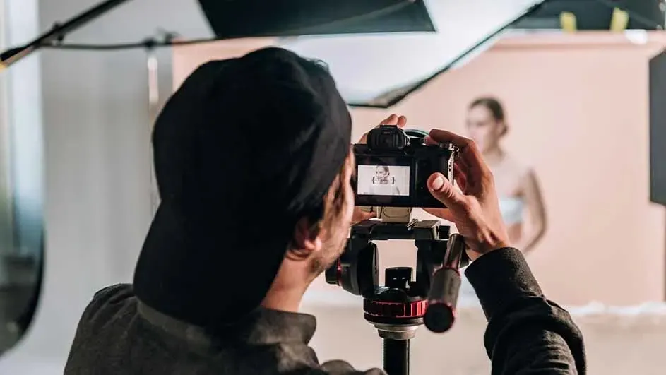 Un photographe prend une photo d'une personne devant un fond beige dans un studio avec un appareil photo sur un trépied.