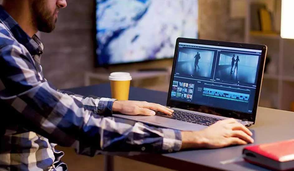 Un ordinateur portable affichant un logiciel de montage vidéo sur une table grise, avec une tasse jaune et un livre rouge à proximité.