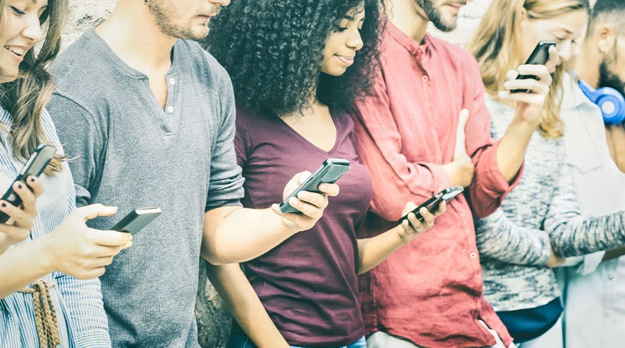 Een rij mensen, elk met een smartphone in de hand, tegen een achtergrond van een gestreepte muur.