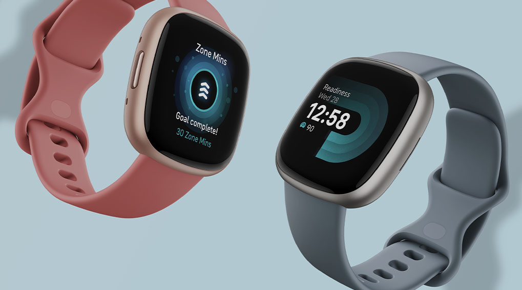 Twee smartwatches met touchscreen. Eén met een roze band en de andere met een grijze band, op een blauwe achtergrond.