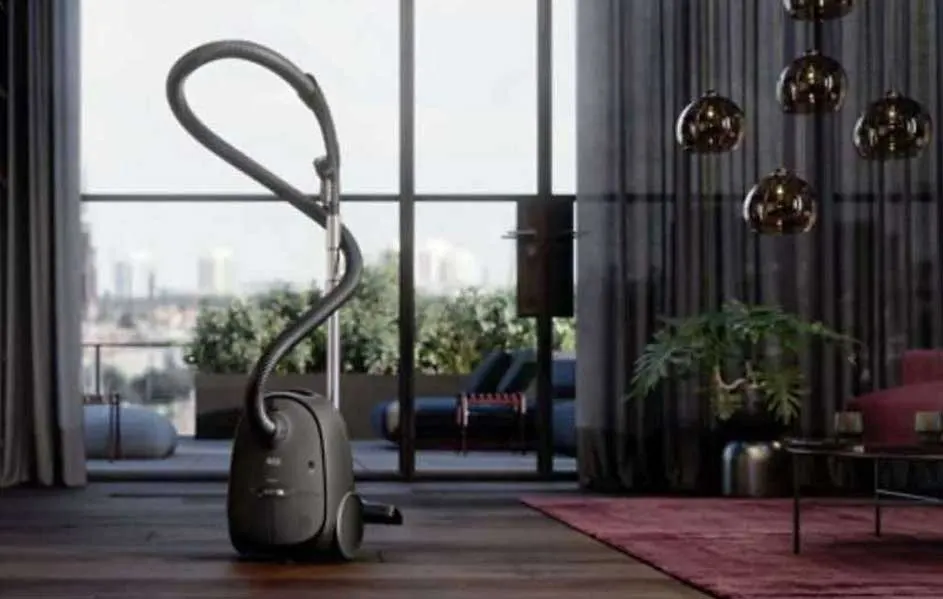 Un aspirateur gris sur un parquet, devant une fenêtre donnant sur un paysage urbain et un intérieur moderne.