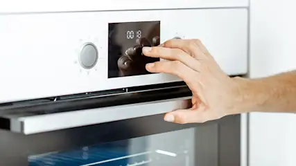 Un four blanc avec un écran noir affichant "00:18". Une main ajuste les réglages près d'un bouton argenté.