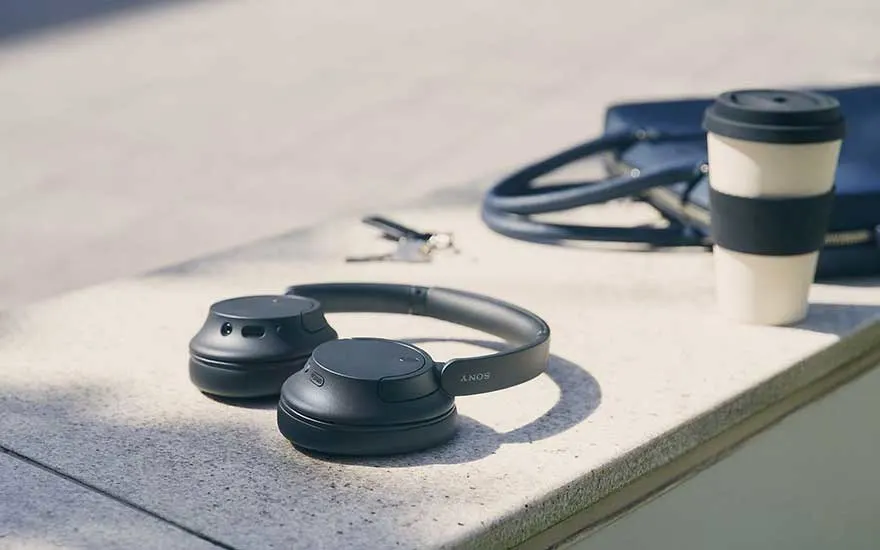 Zwarte Sony koptelefoon op betonnen oppervlak met zachte schaduw, koffiekopje en kabel op de achtergrond. Moderne lifestyle setting.