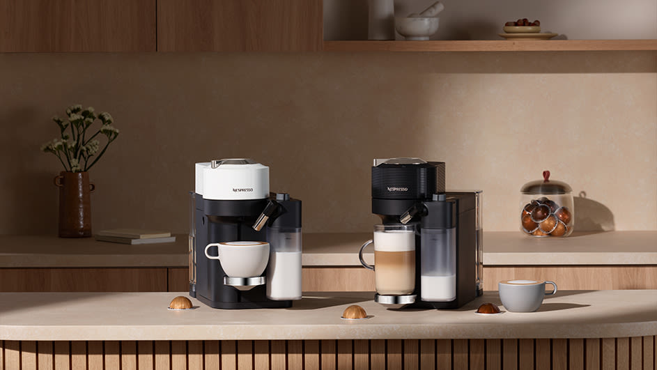 Twee Nespresso koffiemachines, een witte en een zwarte, staan op een aanrecht naast kopjes en capsules.