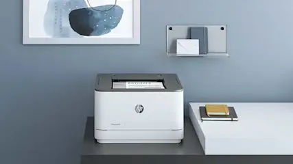 Een witte HP-printer staat op een grijs oppervlak met een blauwe muur op de achtergrond.