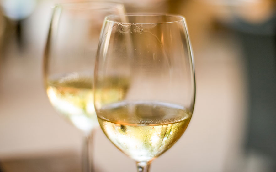 Deux verres à vin remplis d'un liquide jaune clair, probablement du vin blanc, sur fond flou.