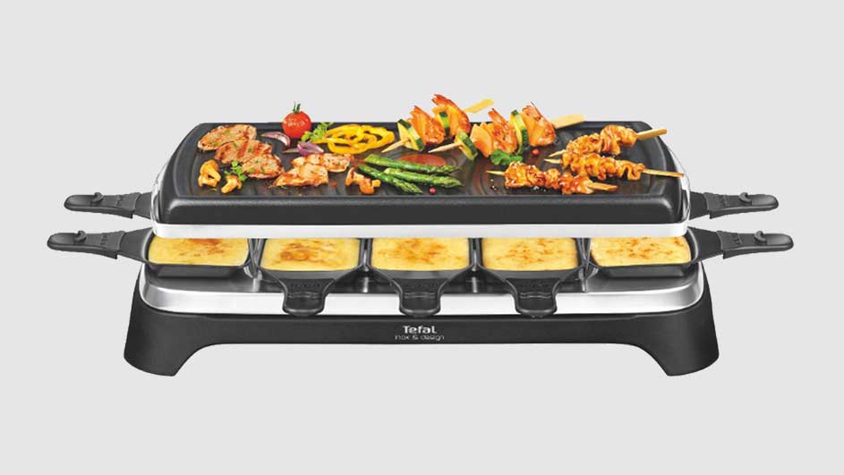 Raclette-grill met vlees, groenten, en kaas. Zwarte grill met zilveren accenten tegen een witte achtergrond.