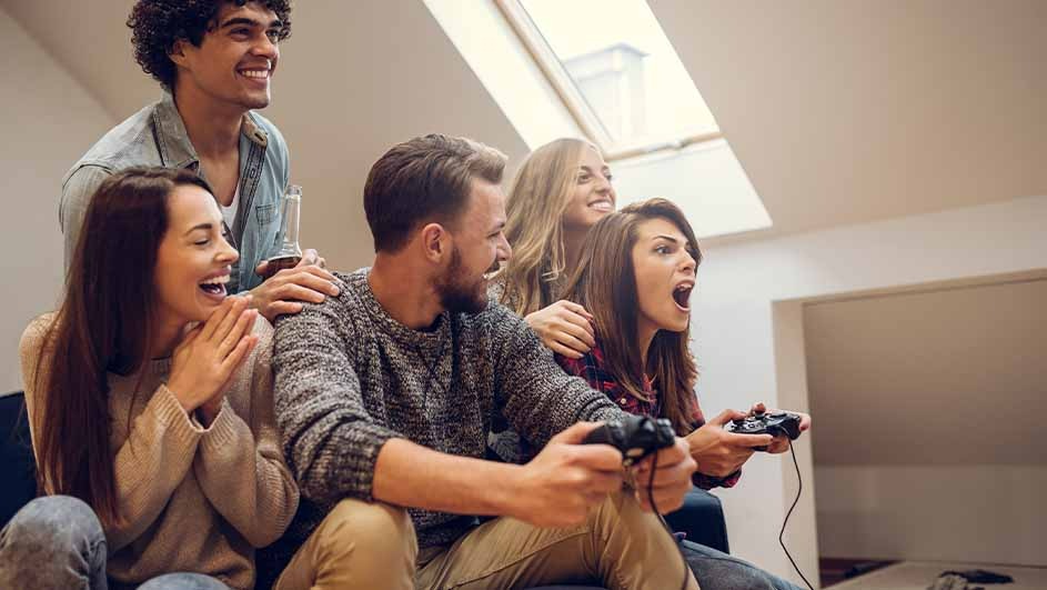 Un groupe joue à des jeux vidéo avec des contrôleurs. Les murs sont beiges et il y a une fenêtre de toit.