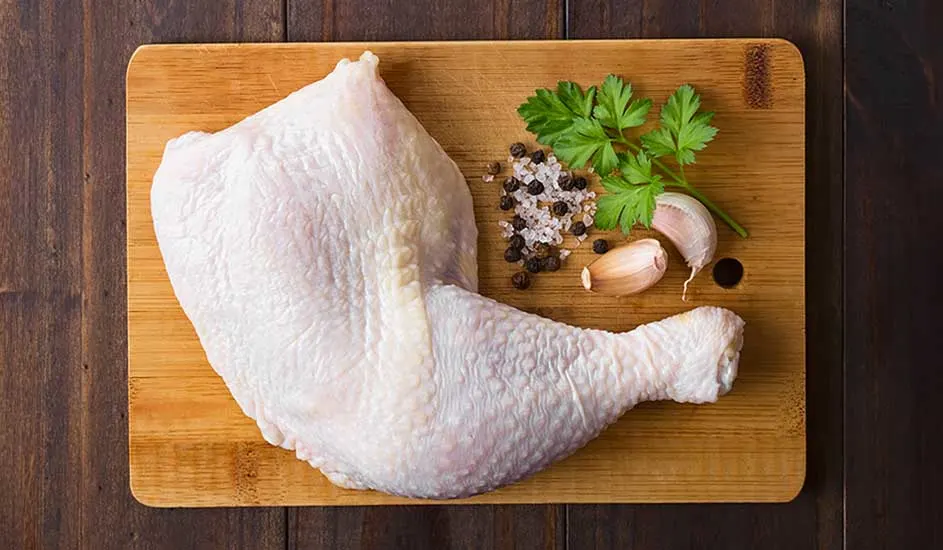 Un morceau de poulet cru sur une planche à découper en bois, avec du persil, de l'ail, du sel et du poivre.