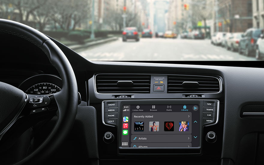 Vue de l'intérieur d'une voiture, tableau de bord noir avec écran tactile affichant des options audio, route urbaine floue en arrière-plan.