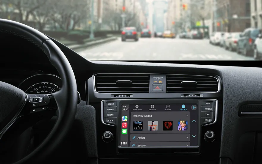 Zicht vanuit een auto op een stadsstraat. Het dashboard toont een scherm met muziekopties. Auto's rijden in de verte.