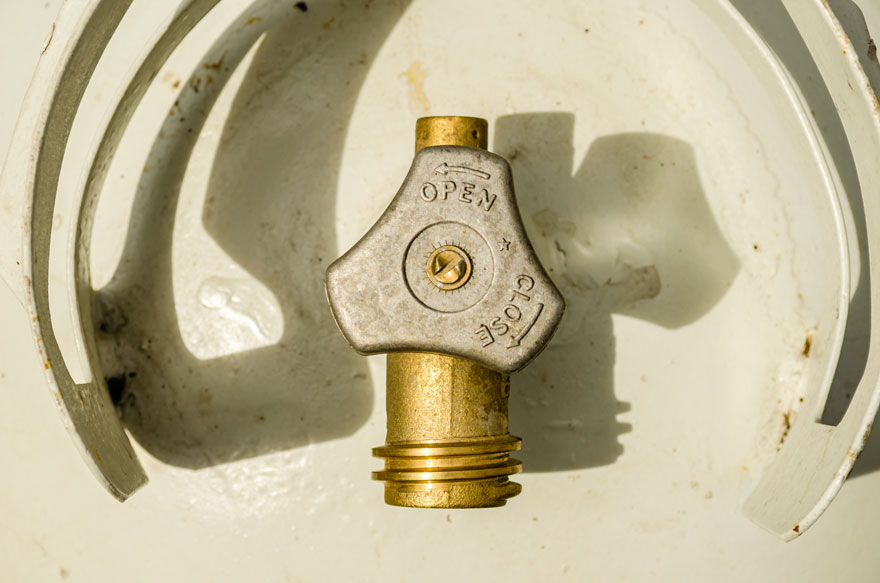 Grijze kraan met 'open' en 'close' op een witte gasfles. De kraan is goudkleurig aan de onderkant.