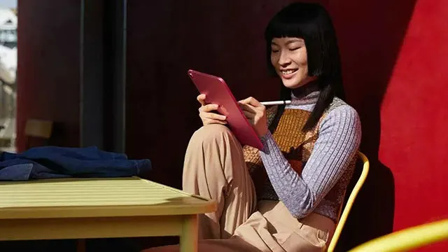 Een rode tablet wordt gebruikt met een witte stylus, zittend aan een gele tafel en stoel, met een rode achtergrond.