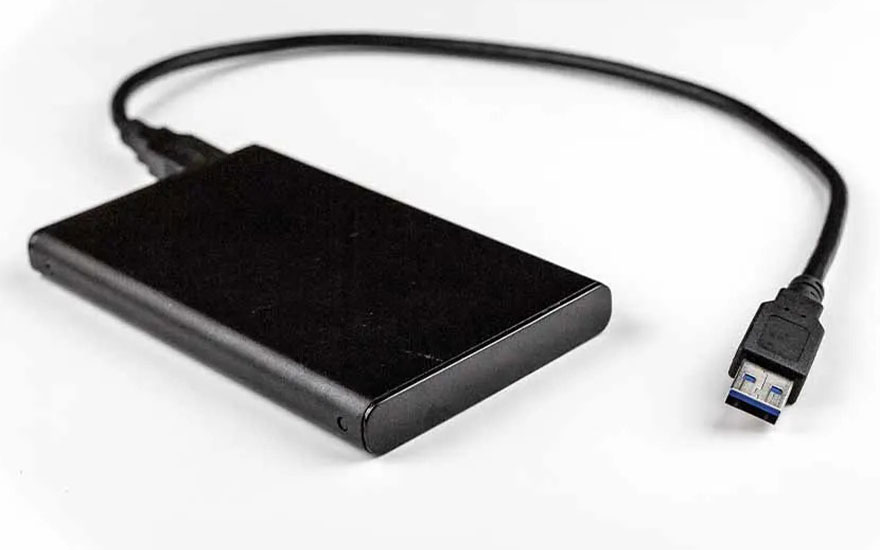 Un disque dur externe noir avec un câble USB 3.0 repose sur un fond blanc, prêt à être connecté à un appareil.