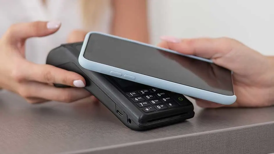 Un téléphone sur un terminal de paiement noir, sur une surface grise. Le téléphone est bleu clair.