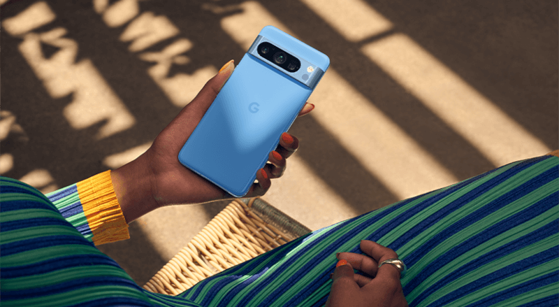 Gros plan d'un téléphone bleu tenu à la main, avec un appareil photo à l'arrière. Assise sur une chaise en osier.