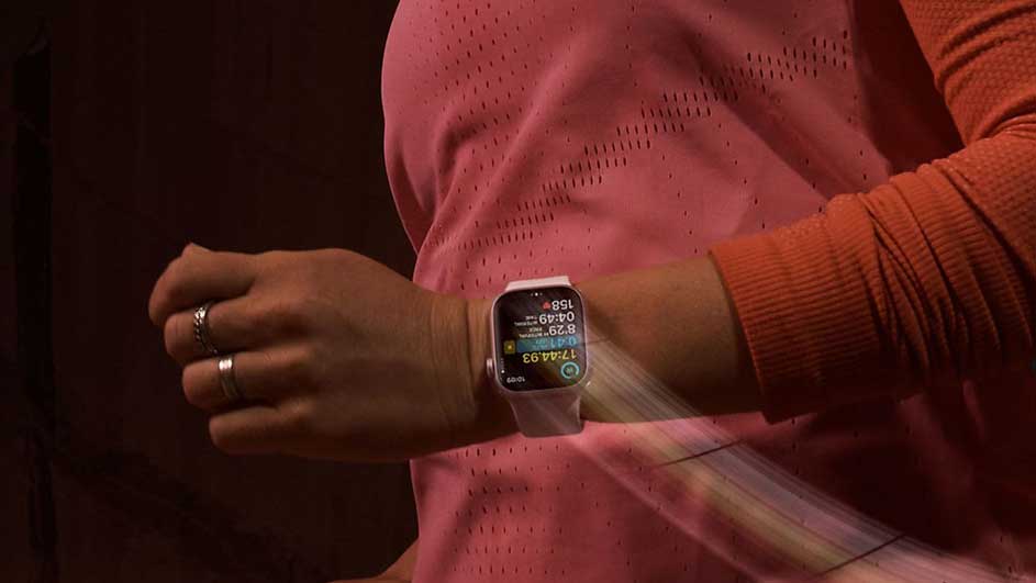 Poignet avec une montre numérique affichant des données. Le sujet porte un haut rose à trous et une manche orange.