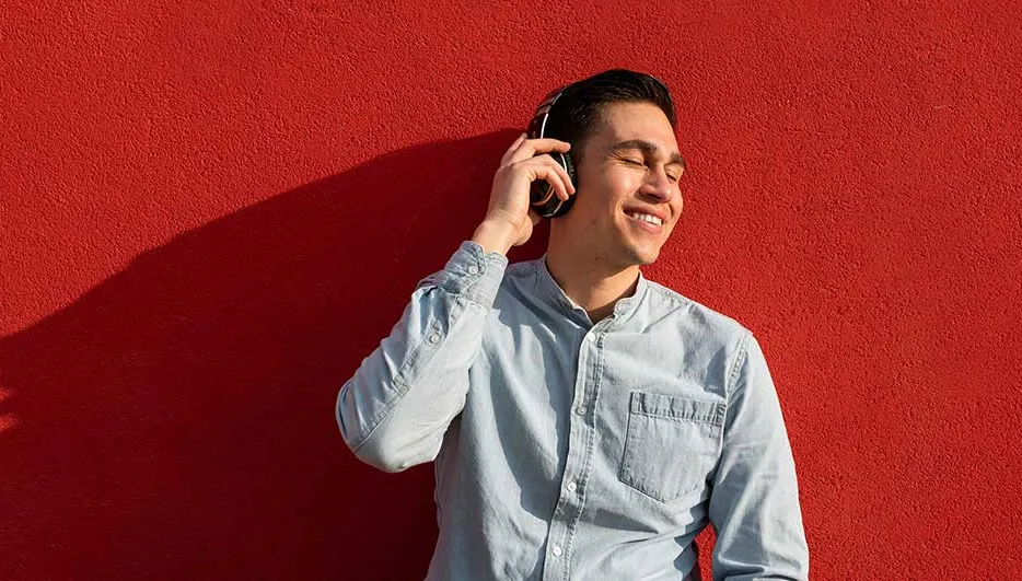 Un mur rouge sert de fond à une personne qui écoute de la musique avec des écouteurs.