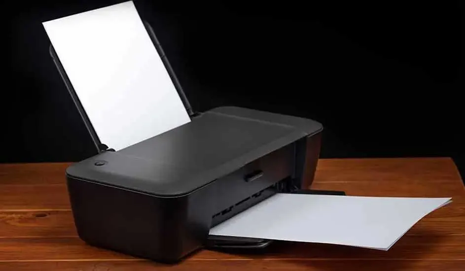 Une imprimante noire est posée sur une table en bois avec du papier blanc à l'intérieur. Fond noir.