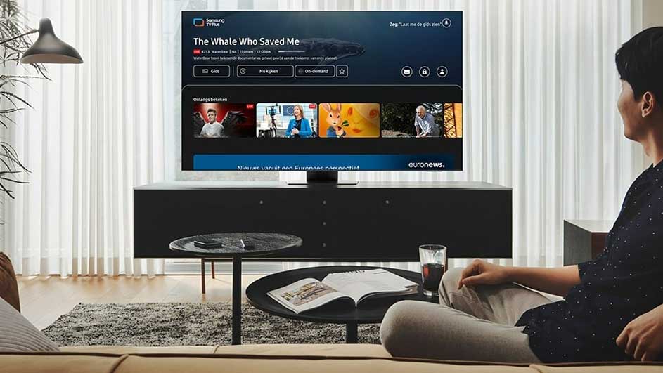 Salon avec téléviseur affichant un menu de diffusion en continu sur un meuble noir, table basse avec livre et boisson.