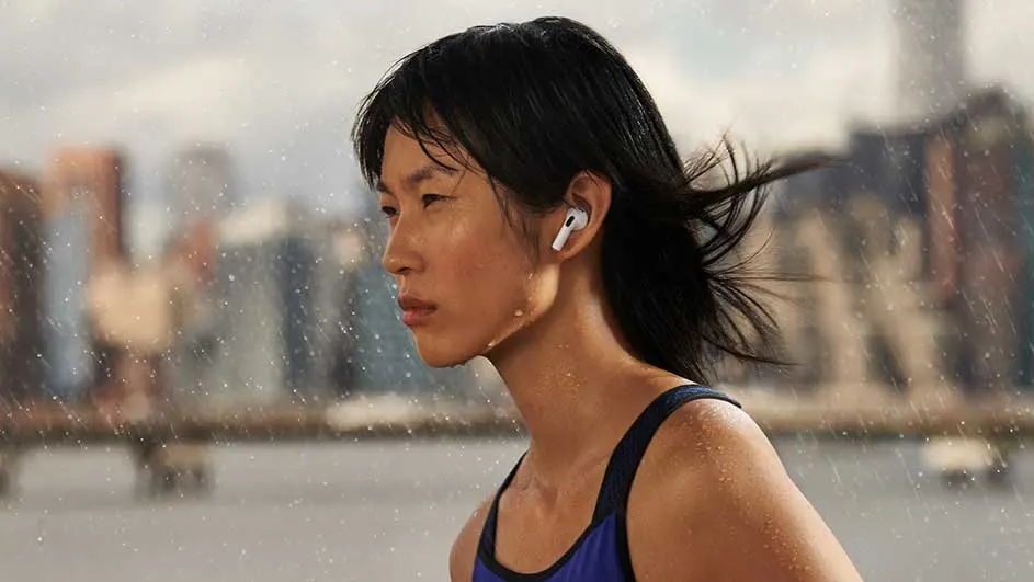 Een close-up van een wit oortje in een oor, met op de achtergrond een vage stedelijke omgeving in de regen.