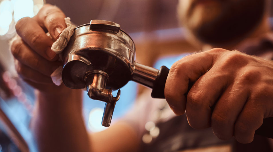 Un barista nettoie un porte-filtre à café en métal argenté avec un chiffon blanc dans un café.