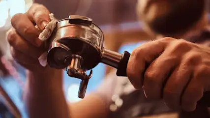 Un barista nettoie un porte-filtre à café en métal argenté avec un chiffon blanc dans un café.