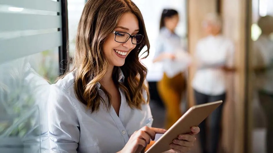 Une femme utilise une tablette dans un bureau. D'autres personnes sont visibles en arrière-plan.