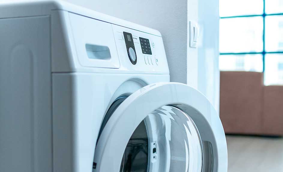 Close-up of an open, white washing machine with a digital control panel, set against a light wall, and boxes near a window.