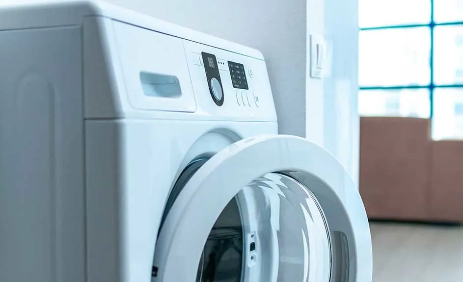 Close-up of an open, white washing machine with a digital control panel, set against a light wall, and boxes near a window.
