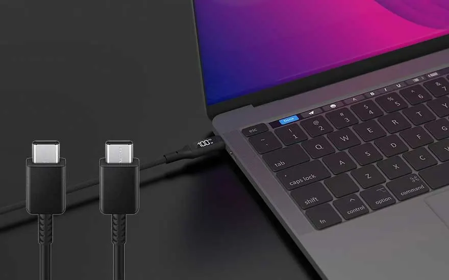 Een zwarte USB-C-kabel is aangesloten op een laptop, die 100% opgeladen is. Het laptopscherm is paars.