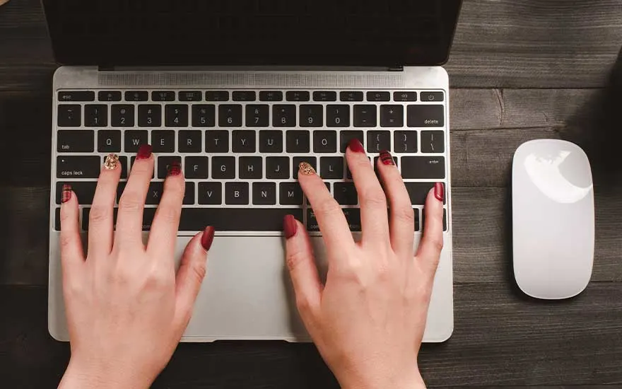 Vue du dessus d'un clavier d'ordinateur portable argenté et d'une souris blanche sur une table en bois sombre.