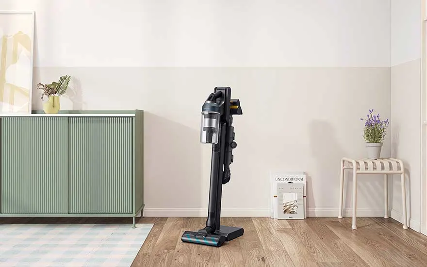 Aspirateur balai vertical sur support autonome dans un salon serein, près d’un meuble vert, d’un tapis pastel et de discrètes décorations.