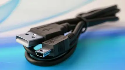 Een zwarte USB-kabel ligt op een blauw-wit oppervlak, met een USB-A en een mini-USB connector zichtbaar.
