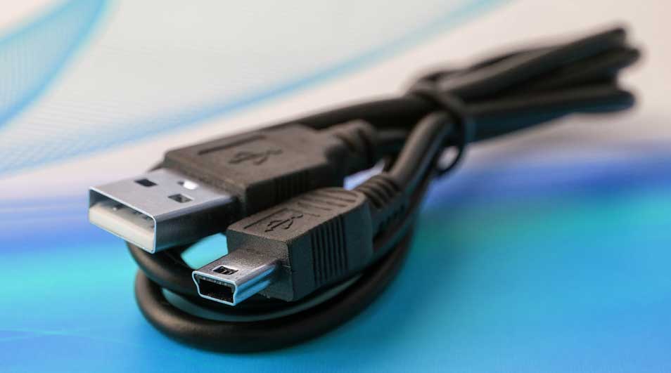 Un câble USB noir enroulé repose sur un fond bleu et blanc. Les extrémités du câble sont visibles.