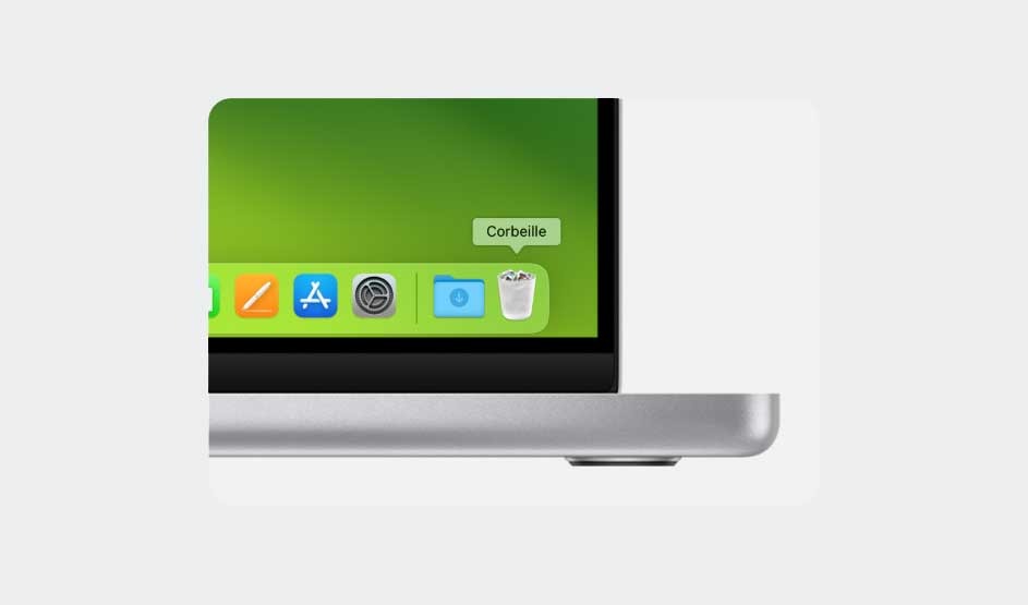 Close-up of an Apple MacBook corner showing the Dock on a green desktop, with the Trash labelled “Corbeille”, apps, and the sleek silver chassis.