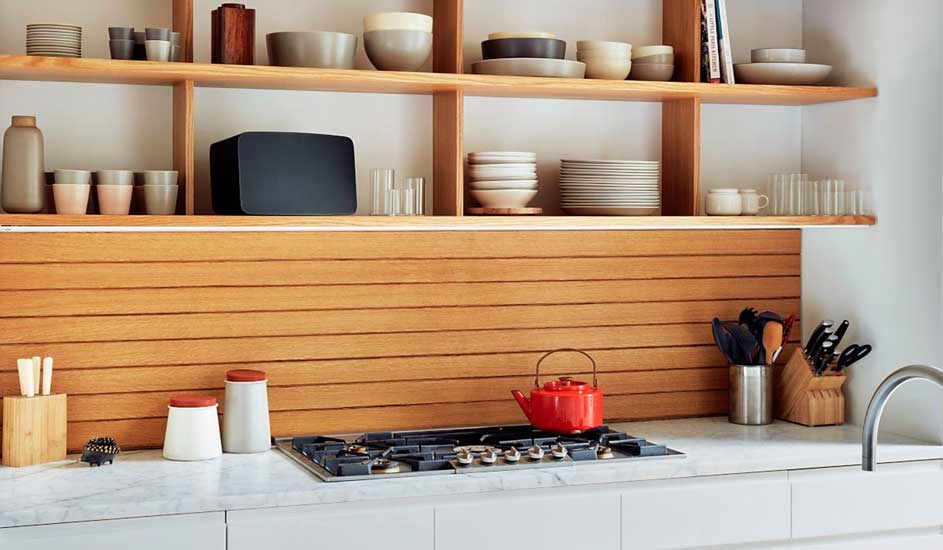 Een keuken met houten rekken vol servies, een houten achterwand, een kookplaat met rode ketel en keukengerei.