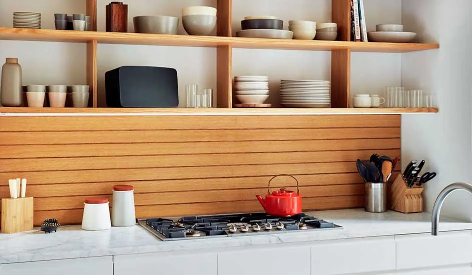 Een keuken met houten rekken vol servies, een houten achterwand, een kookplaat met rode ketel en keukengerei.