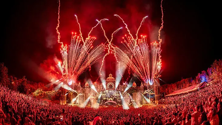 Groot festivalpubliek kijkt naar vuurwerk boven een verlicht podium.