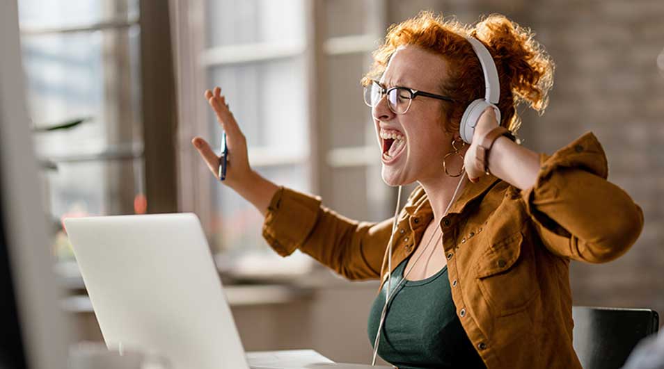 Une personne utilise un ordinateur portable blanc avec un casque blanc dans un bureau lumineux.