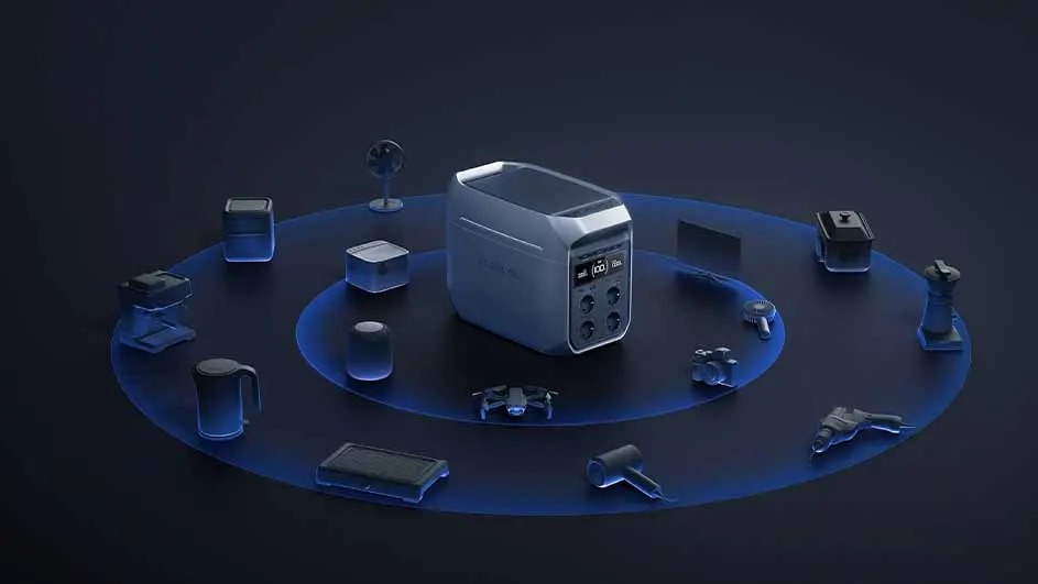A gray portable power station sits on a dark surface. Several small objects like a fan, drone, and solar panel surround it.