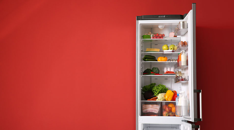 Un réfrigérateur blanc ouvert, rempli de fruits et légumes colorés, sur fond rouge uni.