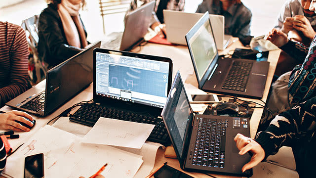 Une table avec plusieurs ordinateurs portables ouverts, des papiers, des stylos et des téléphones portables.