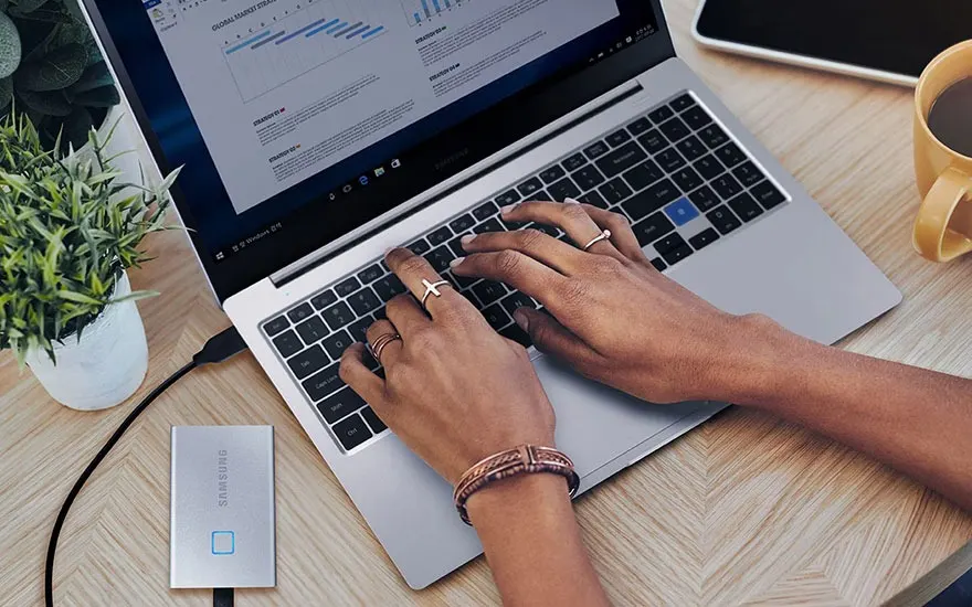 Een laptop met een grafiek op het scherm staat op een houten tafel. Een externe harde schijf is aangesloten.