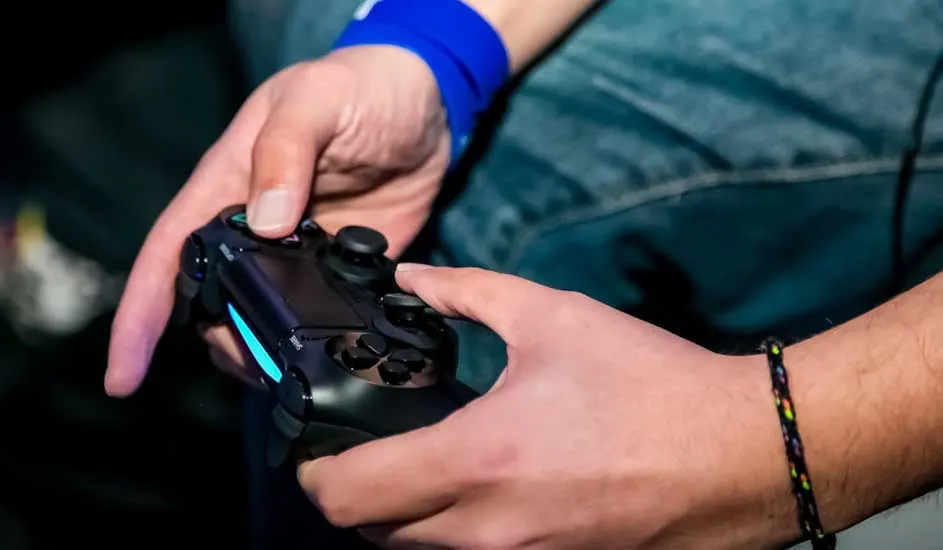 Een persoon houdt een zwarte PlayStation-controller vast met blauwe accenten. De achtergrond is donker.