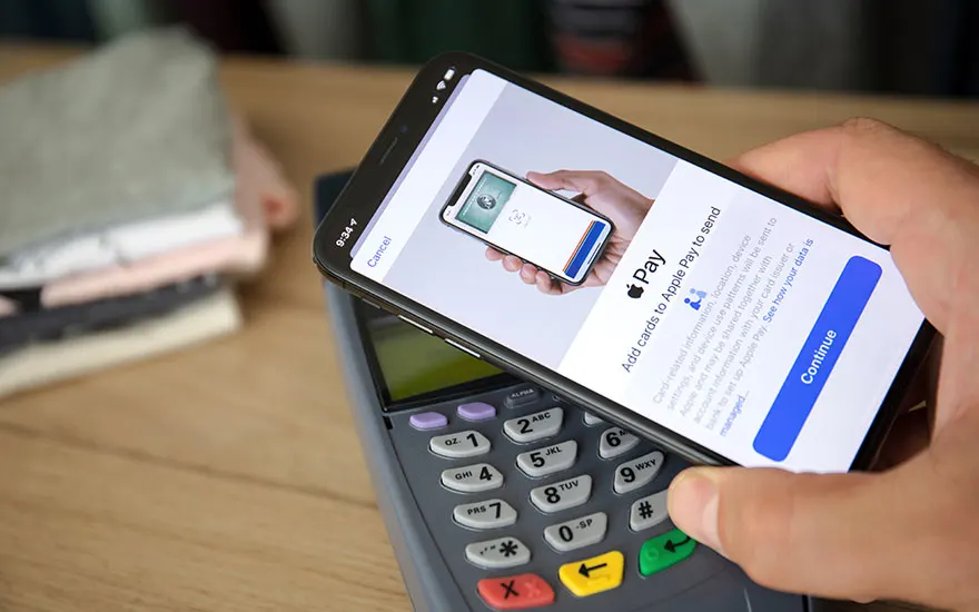 Un téléphone avec Apple Pay sur un terminal de paiement. Boutons numériques et touches colorées visibles.