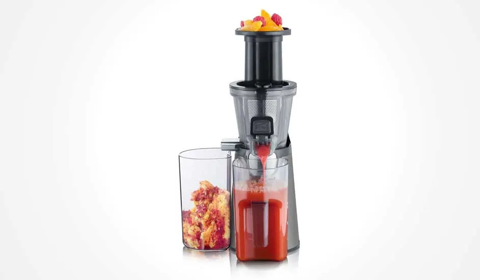 Une centrifugeuse presse des morceaux de fruits en jus frais rouge, versé dans un verre, la pulpe est récupérée à part dans un récipient.