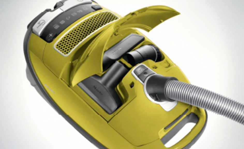 Un aspirateur jaune avec un tuyau gris est ouvert, révélant des accessoires noirs à l'intérieur.